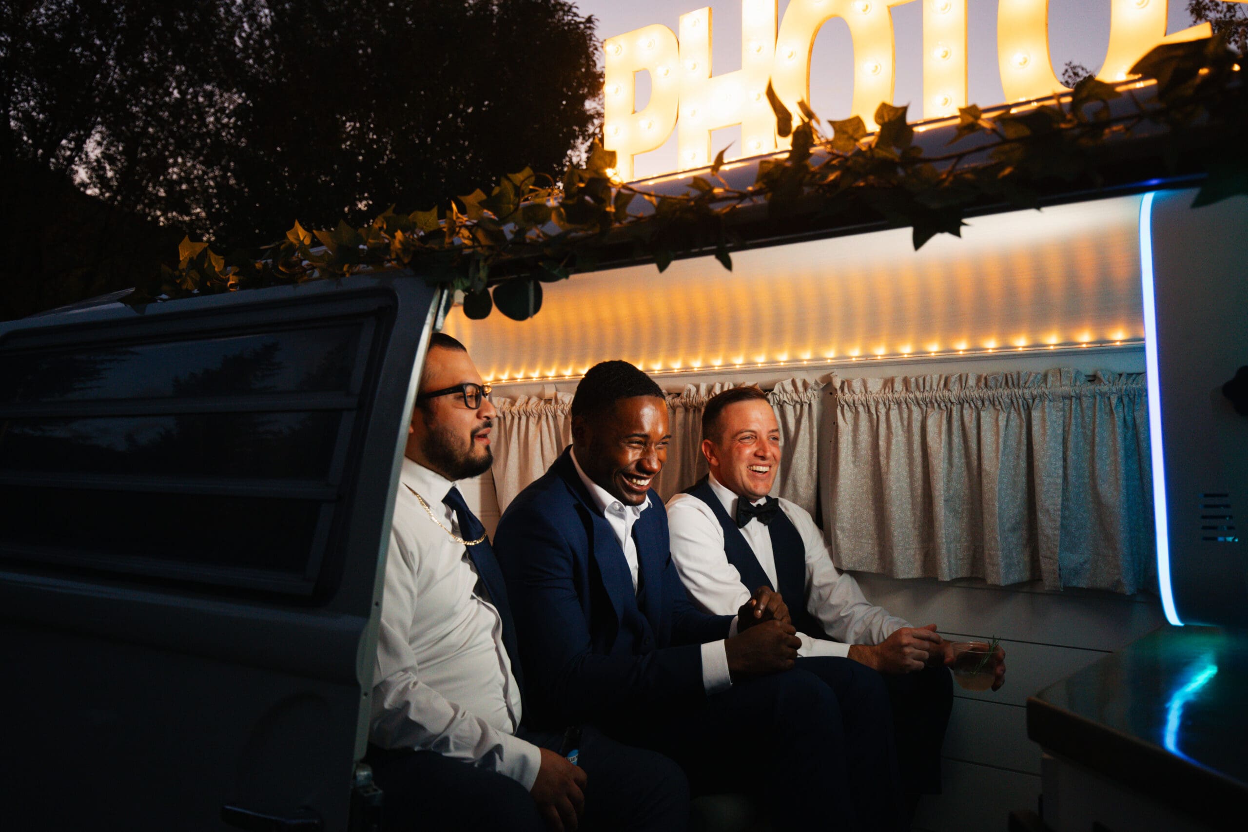 Three groomsmen sitting in the Denver Photo Bus smiling at the photo booth camera